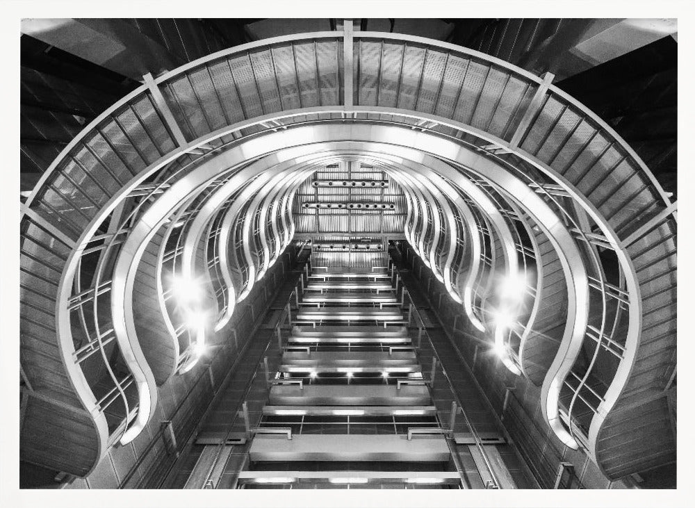 A symmetrical, low-angle black and white photograph of a futuristic escalator or grand staircase. The structure features illuminated, repeating curved arches on both sides, creating a tunnel-like perspective leading upwards. The image is presented within a silver-colored frame. Artwork
