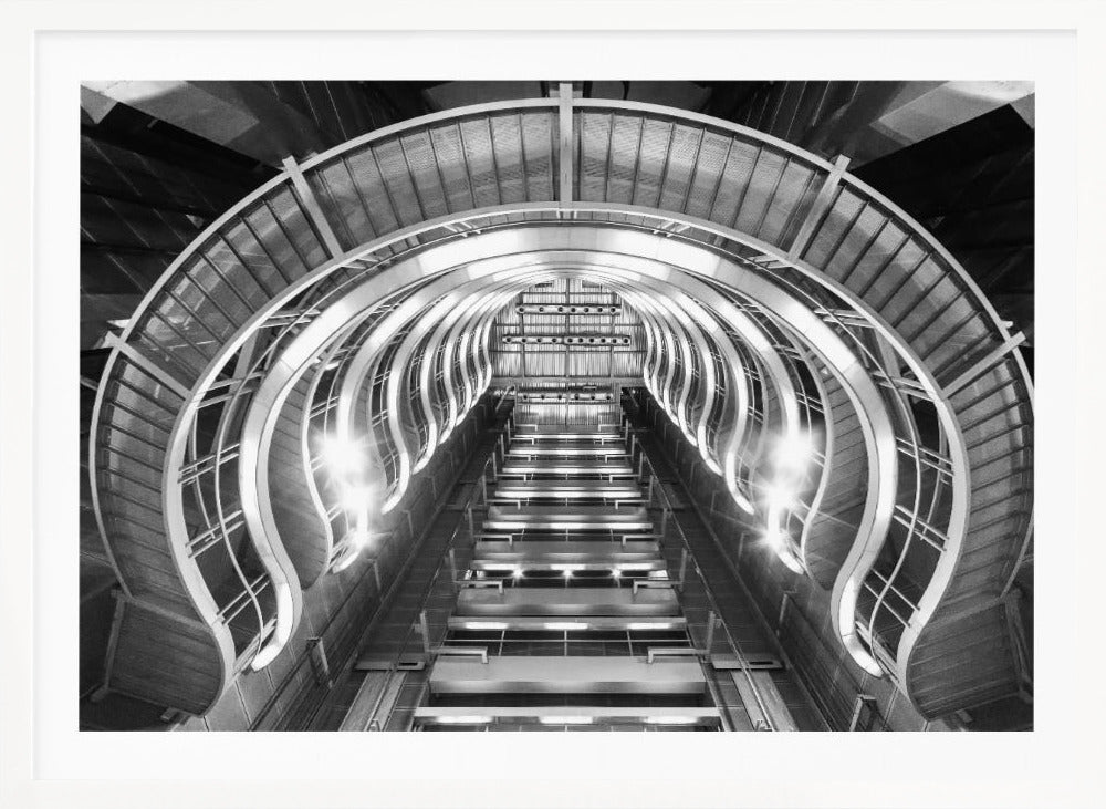 A symmetrical, low-angle black and white photograph of a futuristic escalator or grand staircase. The structure features illuminated, repeating curved arches on both sides, creating a tunnel-like perspective leading upwards. The image is presented within a silver-colored frame. Artwork