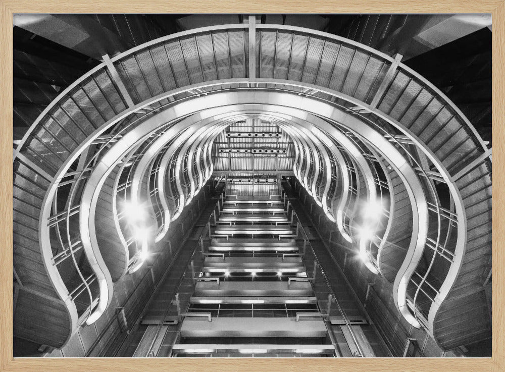 A symmetrical, low-angle black and white photograph of a futuristic escalator or grand staircase. The structure features illuminated, repeating curved arches on both sides, creating a tunnel-like perspective leading upwards. The image is presented within a silver-colored frame. Artwork