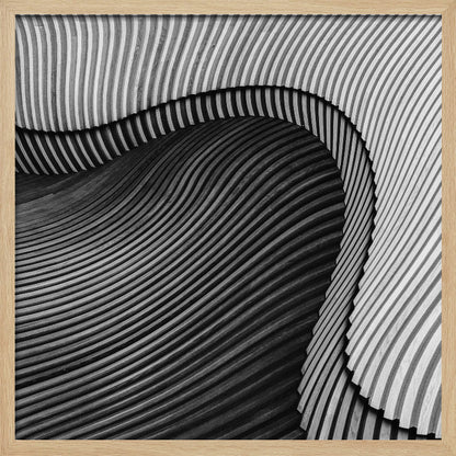 A square, black and white abstract photograph in a light wood frame. The image features layers of flowing, curved surfaces with parallel grooves, creating a strong sense of texture and depth. Lighter, striped layers with vertical lines curve over a darker, undulating section, resembling waves or sculpted wood, drawing the eye into a central dark crevice. Decor