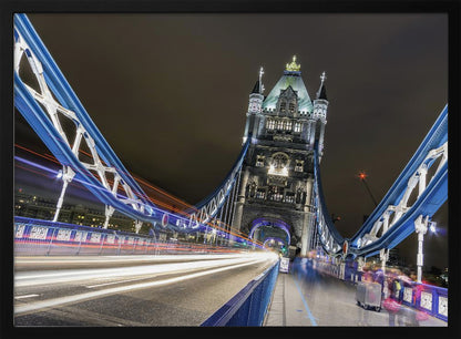 A dramatic, long-exposure night photograph from the deck of London's Tower Bridge, showing vibrant blue support structures curving towards an illuminated stone tower against a dark sky, with bright streaks of light from traffic. Wall Art