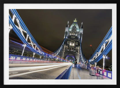 A dramatic, long-exposure night photograph from the deck of London's Tower Bridge, showing vibrant blue support structures curving towards an illuminated stone tower against a dark sky, with bright streaks of light from traffic. Wall Art