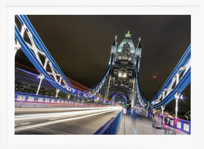 A dramatic, long-exposure night photograph from the deck of London's Tower Bridge, showing vibrant blue support structures curving towards an illuminated stone tower against a dark sky, with bright streaks of light from traffic. Wall Art