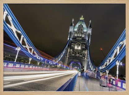 A dramatic, long-exposure night photograph from the deck of London's Tower Bridge, showing vibrant blue support structures curving towards an illuminated stone tower against a dark sky, with bright streaks of light from traffic. Wall Art