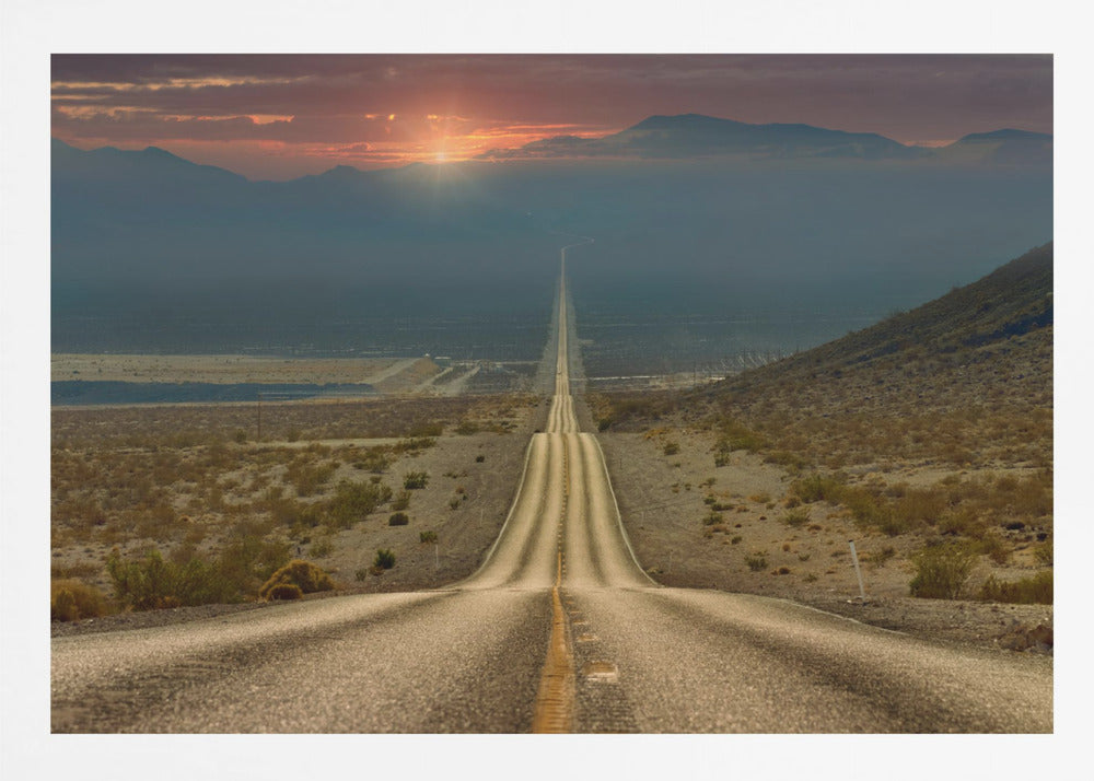 A high-angle view of a long, straight, and hilly road disappearing into the horizon of a vast desert valley at sunset, with mountains in the background under a warm, glowing sky, all enclosed in a silver frame. Poster