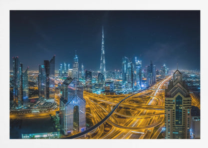 A vibrant aerial photograph of the Dubai skyline at night, with the iconic Burj Khalifa towering in the center. A complex web of brightly lit highways with light trails from traffic dominates the foreground, weaving between modern skyscrapers under a starry night sky. Decor