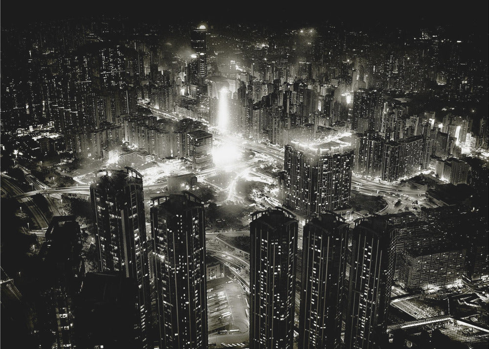 A framed black and white aerial photograph of a dense city at night. The high-angle view captures countless illuminated skyscrapers and winding highways, creating a dramatic and bustling urban landscape. Print