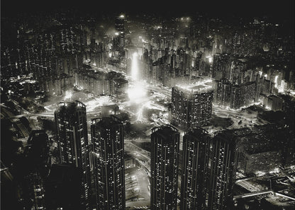 A framed black and white aerial photograph of a dense city at night. The high-angle view captures countless illuminated skyscrapers and winding highways, creating a dramatic and bustling urban landscape. Print