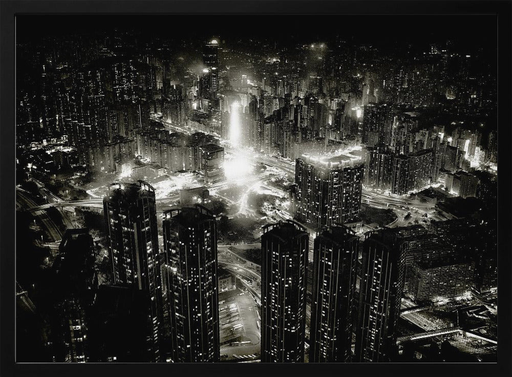A framed black and white aerial photograph of a dense city at night. The high-angle view captures countless illuminated skyscrapers and winding highways, creating a dramatic and bustling urban landscape. Print