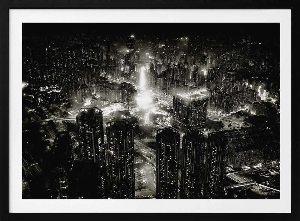 A framed black and white aerial photograph of a dense city at night. The high-angle view captures countless illuminated skyscrapers and winding highways, creating a dramatic and bustling urban landscape. Print