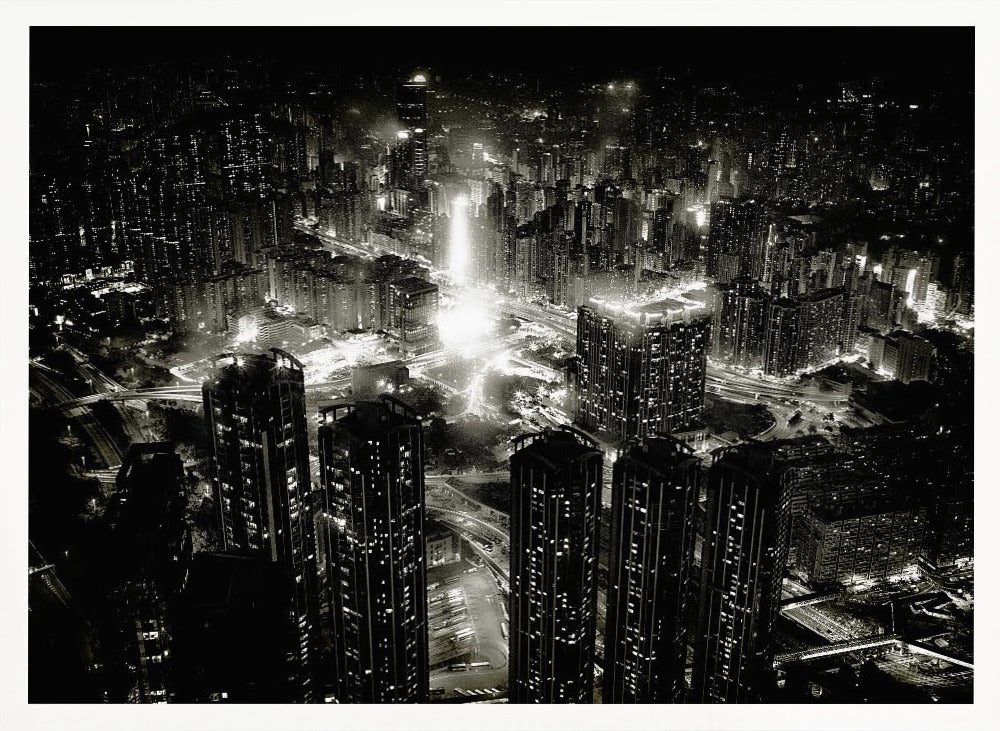 A framed black and white aerial photograph of a dense city at night. The high-angle view captures countless illuminated skyscrapers and winding highways, creating a dramatic and bustling urban landscape. Print