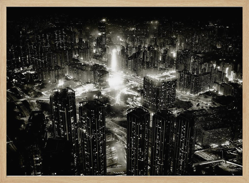 A framed black and white aerial photograph of a dense city at night. The high-angle view captures countless illuminated skyscrapers and winding highways, creating a dramatic and bustling urban landscape. Print