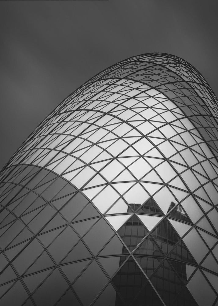 A framed, low-angle, black and white photograph of the curved, glass-paneled facade of a modern skyscraper, creating a dynamic pattern of reflective diamonds against a dark, moody sky. Artwork
