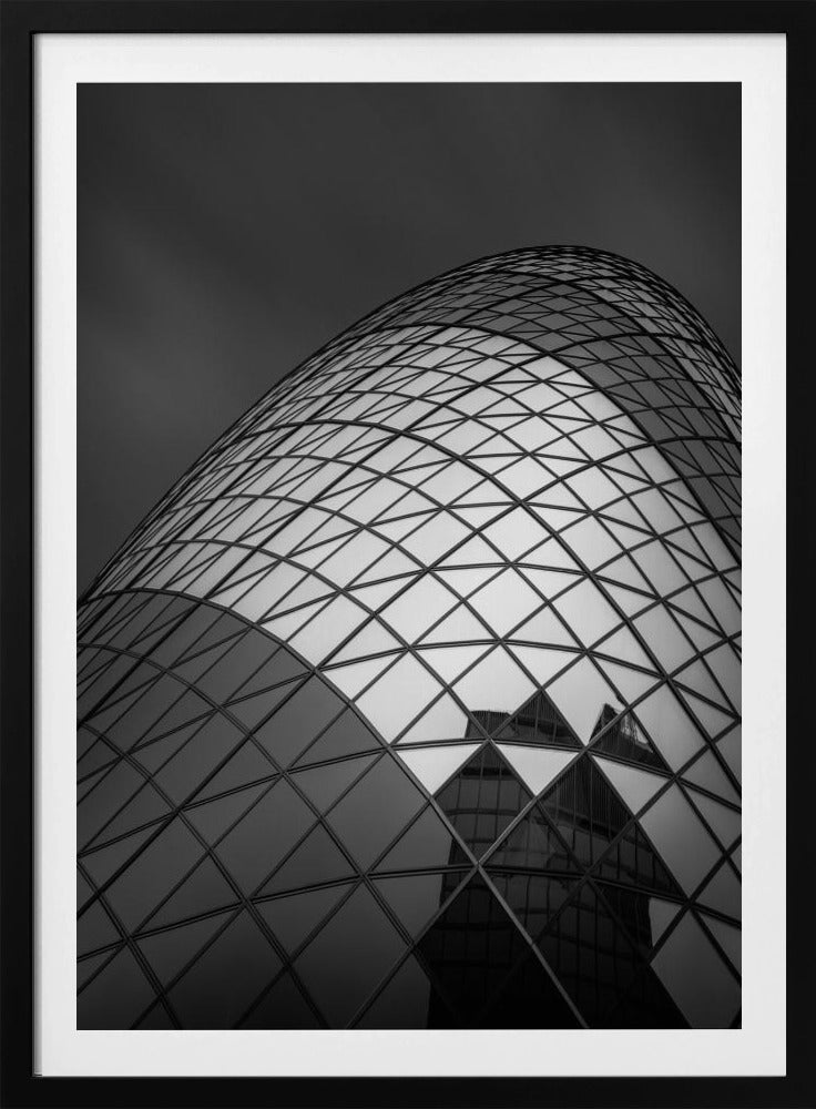 A framed, low-angle, black and white photograph of the curved, glass-paneled facade of a modern skyscraper, creating a dynamic pattern of reflective diamonds against a dark, moody sky. Artwork
