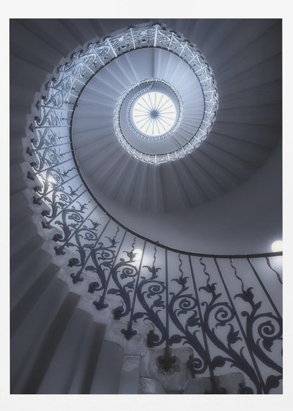 A dramatic low-angle view looking up a majestic spiral staircase, its ornate black wrought iron railings creating a dark, intricate pattern against the cool-toned white steps that wind towards a circular skylight at the apex. Decor