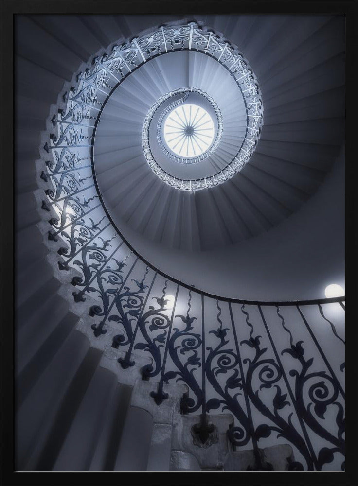 A dramatic low-angle view looking up a majestic spiral staircase, its ornate black wrought iron railings creating a dark, intricate pattern against the cool-toned white steps that wind towards a circular skylight at the apex. Decor