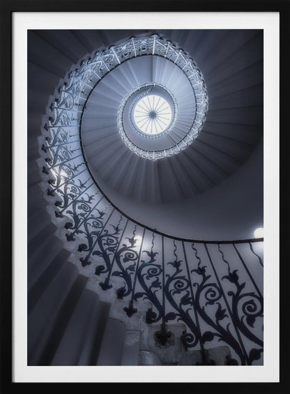 A dramatic low-angle view looking up a majestic spiral staircase, its ornate black wrought iron railings creating a dark, intricate pattern against the cool-toned white steps that wind towards a circular skylight at the apex. Decor