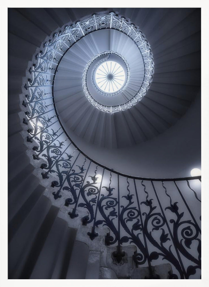 A dramatic low-angle view looking up a majestic spiral staircase, its ornate black wrought iron railings creating a dark, intricate pattern against the cool-toned white steps that wind towards a circular skylight at the apex. Decor
