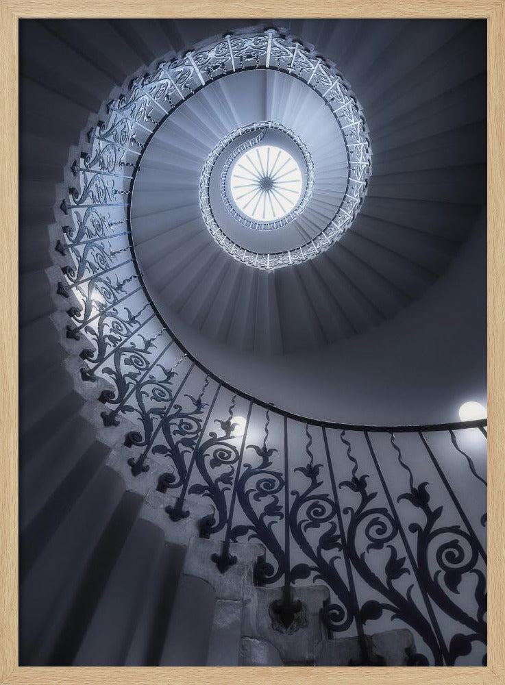 A dramatic low-angle view looking up a majestic spiral staircase, its ornate black wrought iron railings creating a dark, intricate pattern against the cool-toned white steps that wind towards a circular skylight at the apex. Decor