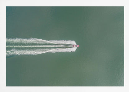 An aerial top-down photograph of a red motorboat speeding across a vast expanse of calm, green water, leaving a long, white, frothy wake behind it. The scene is presented within a simple silver frame. Print