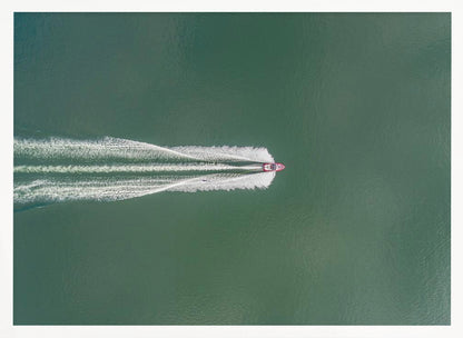 An aerial top-down photograph of a red motorboat speeding across a vast expanse of calm, green water, leaving a long, white, frothy wake behind it. The scene is presented within a simple silver frame. Print
