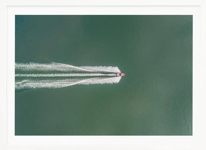 An aerial top-down photograph of a red motorboat speeding across a vast expanse of calm, green water, leaving a long, white, frothy wake behind it. The scene is presented within a simple silver frame. Print