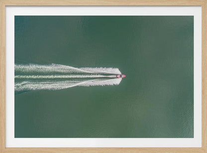 An aerial top-down photograph of a red motorboat speeding across a vast expanse of calm, green water, leaving a long, white, frothy wake behind it. The scene is presented within a simple silver frame. Print