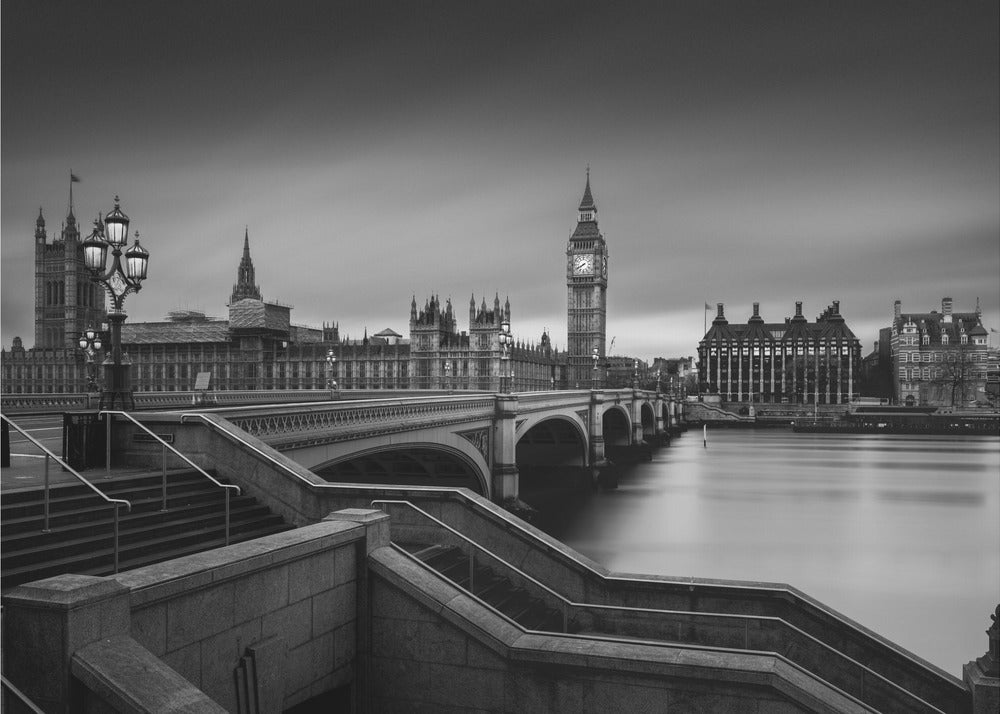 A framed, black and white, long-exposure photograph of the London skyline featuring the Houses of Parliament and the Big Ben clock tower across the River Thames. In the foreground, stone steps lead down towards Westminster Bridge, and the water of the river is smooth and reflective under a dark, cloudy sky. Print