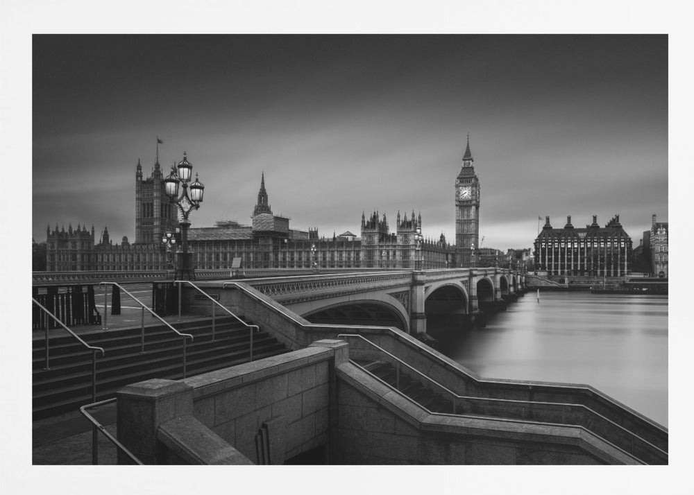 A framed, black and white, long-exposure photograph of the London skyline featuring the Houses of Parliament and the Big Ben clock tower across the River Thames. In the foreground, stone steps lead down towards Westminster Bridge, and the water of the river is smooth and reflective under a dark, cloudy sky. Print