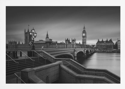 A framed, black and white, long-exposure photograph of the London skyline featuring the Houses of Parliament and the Big Ben clock tower across the River Thames. In the foreground, stone steps lead down towards Westminster Bridge, and the water of the river is smooth and reflective under a dark, cloudy sky. Print