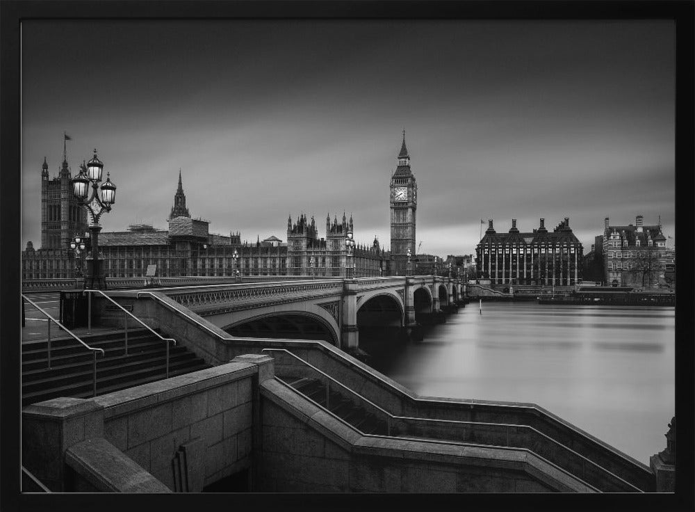 A framed, black and white, long-exposure photograph of the London skyline featuring the Houses of Parliament and the Big Ben clock tower across the River Thames. In the foreground, stone steps lead down towards Westminster Bridge, and the water of the river is smooth and reflective under a dark, cloudy sky. Print