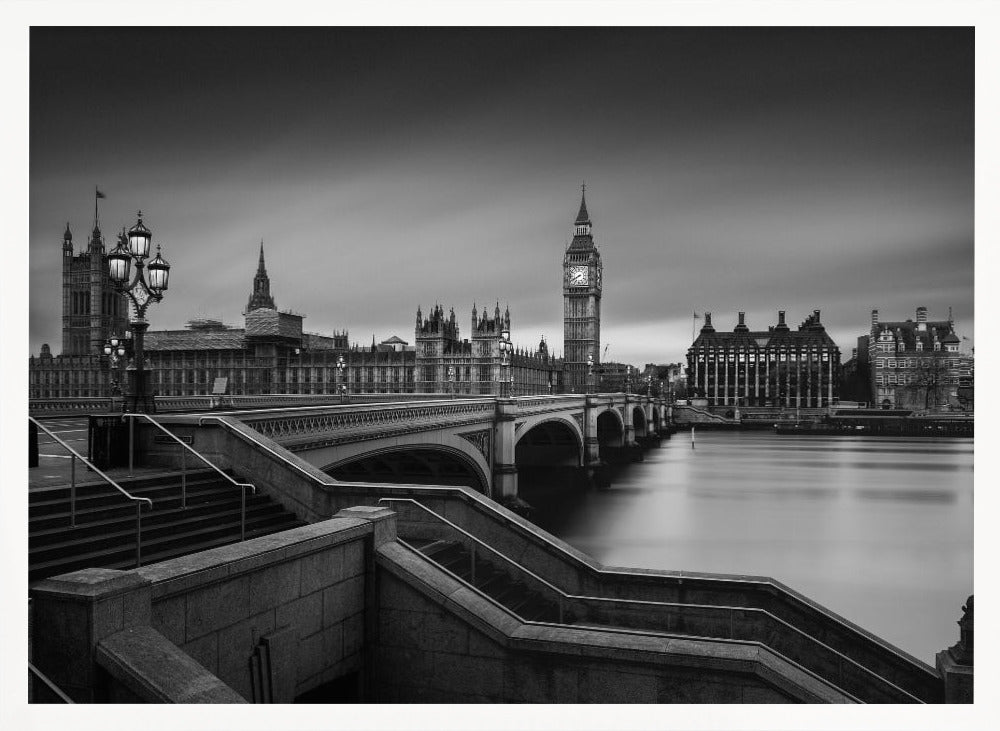 A framed, black and white, long-exposure photograph of the London skyline featuring the Houses of Parliament and the Big Ben clock tower across the River Thames. In the foreground, stone steps lead down towards Westminster Bridge, and the water of the river is smooth and reflective under a dark, cloudy sky. Print