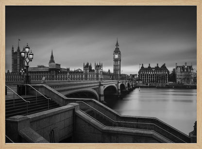 A framed, black and white, long-exposure photograph of the London skyline featuring the Houses of Parliament and the Big Ben clock tower across the River Thames. In the foreground, stone steps lead down towards Westminster Bridge, and the water of the river is smooth and reflective under a dark, cloudy sky. Print