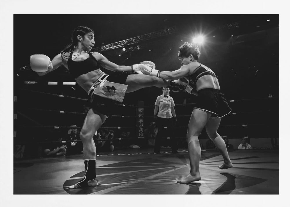 A dramatic black and white action photograph of two female kickboxers in a ring. One fighter, airborne, executes a high kick that connects with the other fighter's gloves, who is bracing for the impact. A referee stands in the background under bright arena lights. Poster