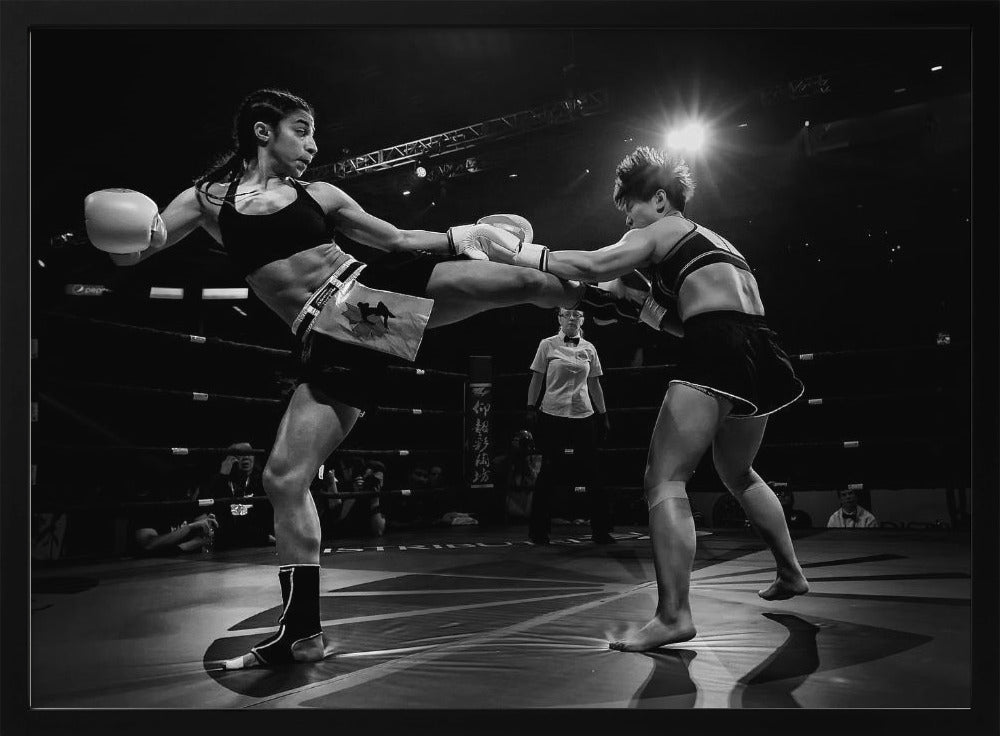 A dramatic black and white action photograph of two female kickboxers in a ring. One fighter, airborne, executes a high kick that connects with the other fighter's gloves, who is bracing for the impact. A referee stands in the background under bright arena lights. Poster