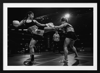 A dramatic black and white action photograph of two female kickboxers in a ring. One fighter, airborne, executes a high kick that connects with the other fighter's gloves, who is bracing for the impact. A referee stands in the background under bright arena lights. Poster