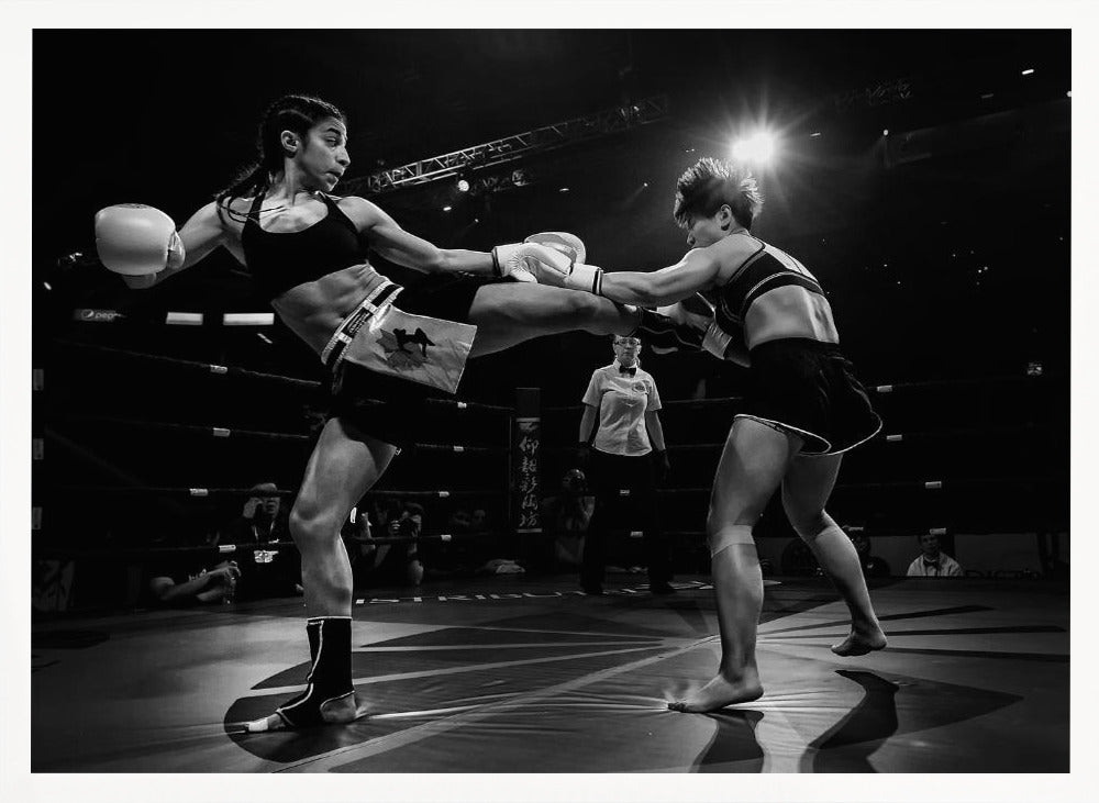 A dramatic black and white action photograph of two female kickboxers in a ring. One fighter, airborne, executes a high kick that connects with the other fighter's gloves, who is bracing for the impact. A referee stands in the background under bright arena lights. Poster