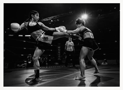 A dramatic black and white action photograph of two female kickboxers in a ring. One fighter, airborne, executes a high kick that connects with the other fighter's gloves, who is bracing for the impact. A referee stands in the background under bright arena lights. Poster