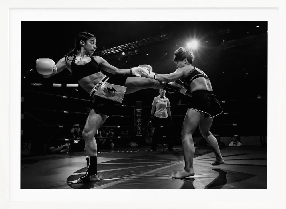 A dramatic black and white action photograph of two female kickboxers in a ring. One fighter, airborne, executes a high kick that connects with the other fighter's gloves, who is bracing for the impact. A referee stands in the background under bright arena lights. Poster