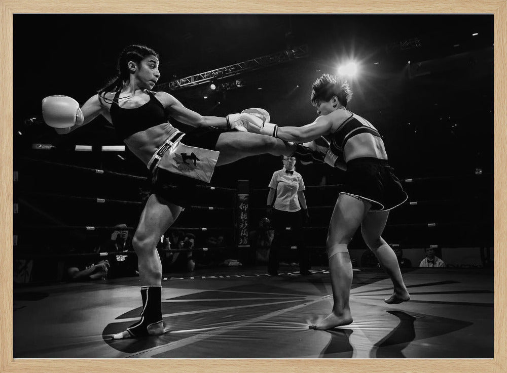 A dramatic black and white action photograph of two female kickboxers in a ring. One fighter, airborne, executes a high kick that connects with the other fighter's gloves, who is bracing for the impact. A referee stands in the background under bright arena lights. Poster