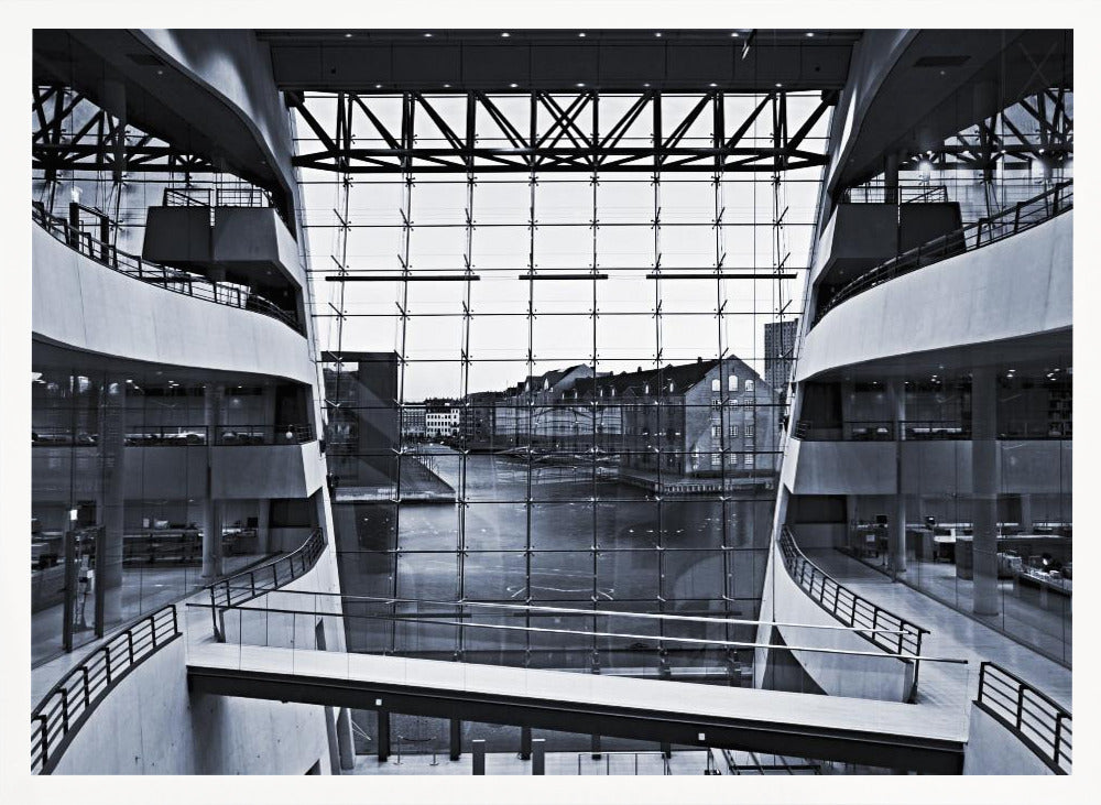 A symmetrical, black and white photograph taken from inside a modern building with curved balconies, looking out through a massive glass wall onto a canal and historic buildings on the opposite bank. A pedestrian bridge crosses the lower part of the frame. Decor