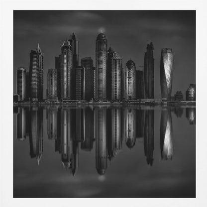 A dramatic black and white photograph of a modern city skyline at night, its towering skyscrapers perfectly reflected in the calm water below, all enclosed within a light brown wooden frame. Print