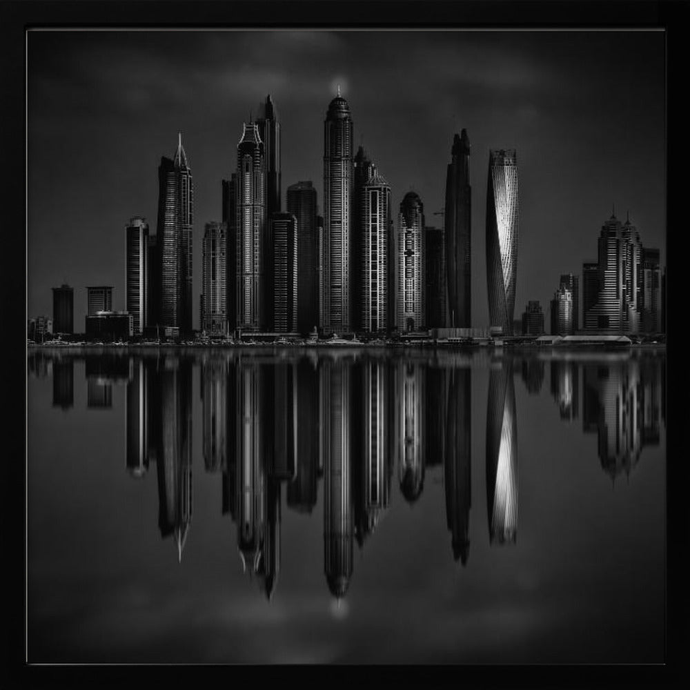 A dramatic black and white photograph of a modern city skyline at night, its towering skyscrapers perfectly reflected in the calm water below, all enclosed within a light brown wooden frame. Print