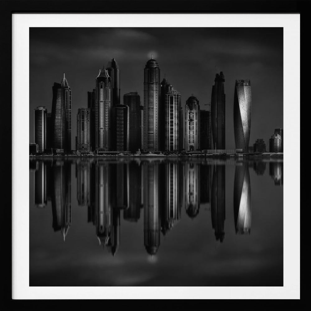 A dramatic black and white photograph of a modern city skyline at night, its towering skyscrapers perfectly reflected in the calm water below, all enclosed within a light brown wooden frame. Print