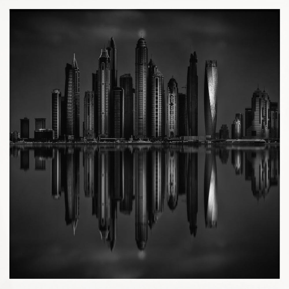 A dramatic black and white photograph of a modern city skyline at night, its towering skyscrapers perfectly reflected in the calm water below, all enclosed within a light brown wooden frame. Print
