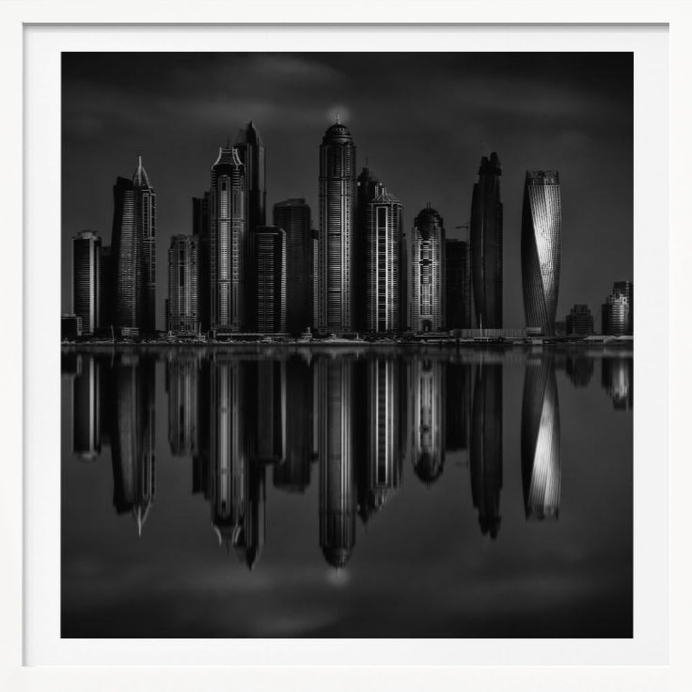 A dramatic black and white photograph of a modern city skyline at night, its towering skyscrapers perfectly reflected in the calm water below, all enclosed within a light brown wooden frame. Print