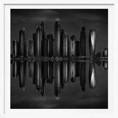 A dramatic black and white photograph of a modern city skyline at night, its towering skyscrapers perfectly reflected in the calm water below, all enclosed within a light brown wooden frame. Print