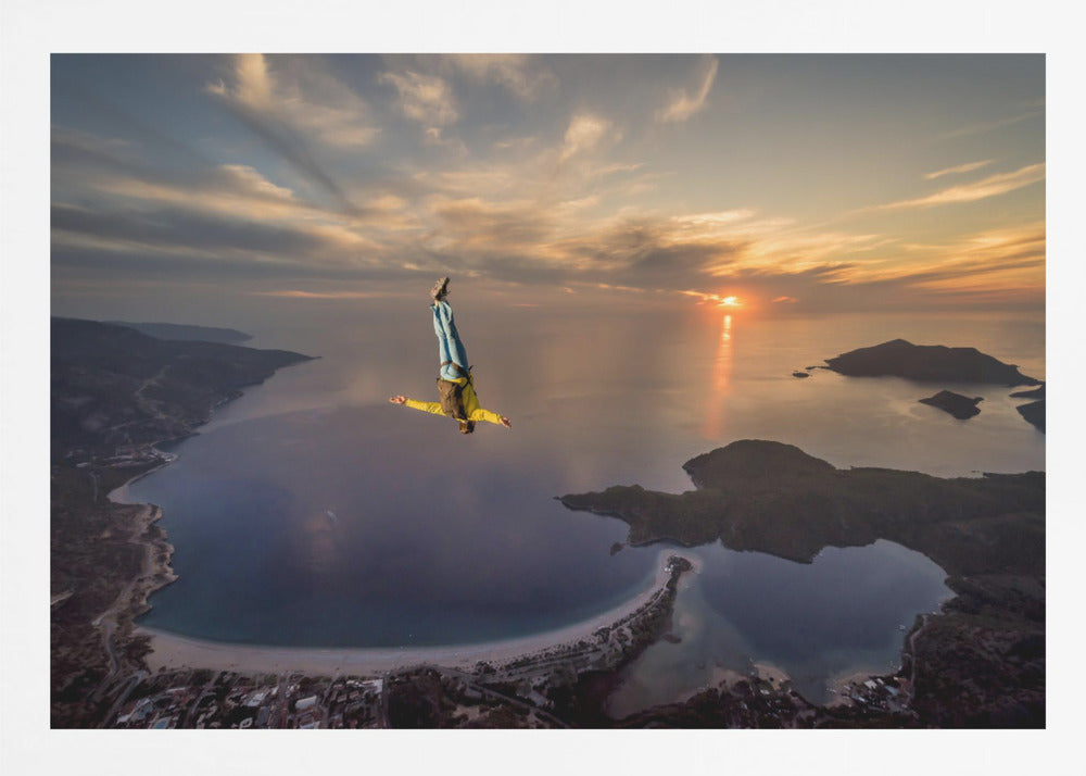 A breathtaking aerial view of a skydiver in a head-down position, freefalling over a vast coastal bay at sunset. The setting sun casts a golden glow over the ocean and clouds, highlighting the islands and coastline below. Decor