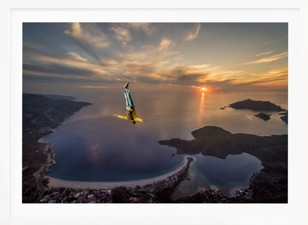 A breathtaking aerial view of a skydiver in a head-down position, freefalling over a vast coastal bay at sunset. The setting sun casts a golden glow over the ocean and clouds, highlighting the islands and coastline below. Decor