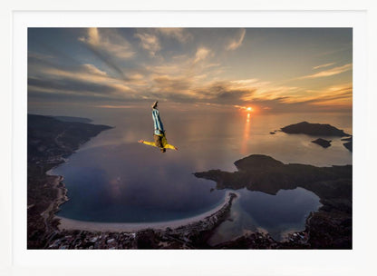 A breathtaking aerial view of a skydiver in a head-down position, freefalling over a vast coastal bay at sunset. The setting sun casts a golden glow over the ocean and clouds, highlighting the islands and coastline below. Decor